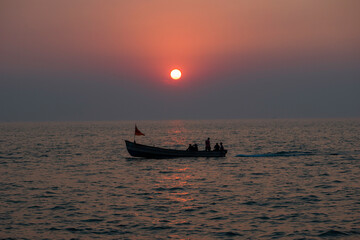 The perfect sunset at the background and the people sailing in the boat in the foreground. 