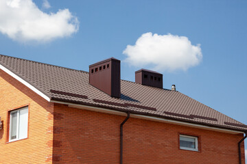 Red metal roof tile and smokestack. Modern chimney on brown roof.