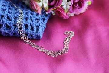 Pulseira cromada, prateada de corações pequenos em fundo de tecido pink e flores artificiais