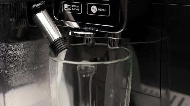 Сlose-up of an automatic coffee machine pouring hot milk into a transparent glass