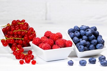 Fresh Raw Berries in white ceramic bowl on white background. Space for text. Red Currant, Raspberry and Blueberry, Summer Fruits
