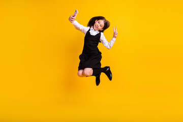 Fototapeta na wymiar Full length body size photo schoolgirl jumping taking selfie showing v-sign isolated vivid yellow color background