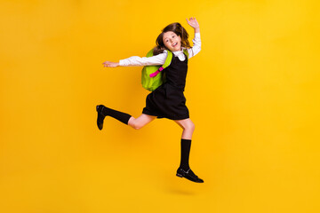 Full length photo of cheerful happy amazed small girl jump up wear backpack isolated on yellow color background