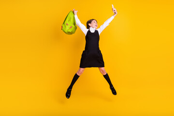 Fototapeta na wymiar Full length body size photo schoolgirl jumping with bag taking selfie isolated vibrant yellow color background