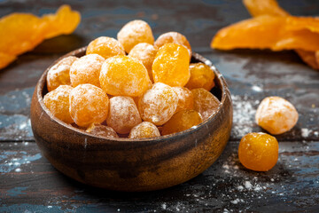 Candied citrus fruits with powdered sugar in a wooden bowl on a dark background. Candied kumquat.