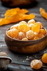Candied citrus fruits with powdered sugar in a wooden bowl on a dark background. Candied kumquat.