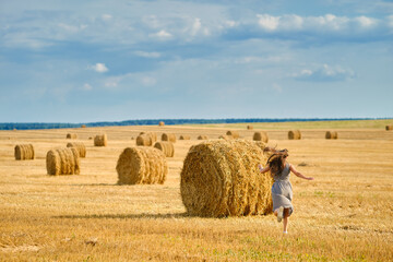 Happy young woman runs to the ricks on the field