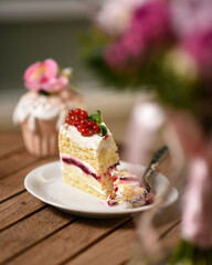 a piece of cake decorated with red berries lies on a white plate on a wooden table in a cafe
