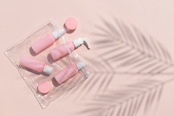 Mock up flatlay with travel size pink cosmetic bottles in bag on beige background. Palm leaves...