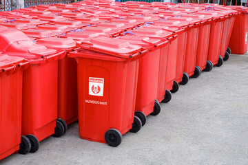 Rows of red hazardous waste bins are neatly packed with rubbish from COVID-19 patients behind the field hospital between waiting to be disposal, Thai language of sign is mean "Hazardous waste"	