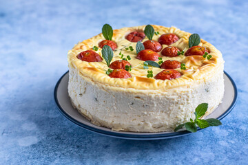 Savoury cheesecake with tomatoes decorated with mint, blue concrete background.