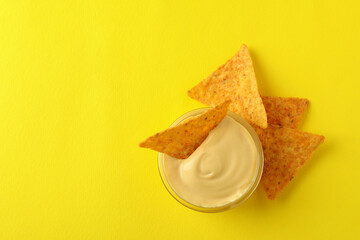 Bowl with cheese sauce and chips on yellow background