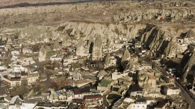 Aerial view of a small town located by the mountain range. Action. Red turkish flag waving on a rock top, sunny village in dry area.