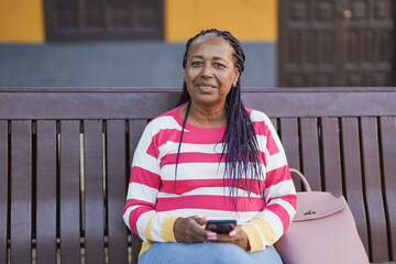 Senior african woman sitting on a bench in the city while holding her smartphone in the hands