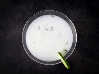 Top view of ayran with dill in glass goblet with cucumber slice on dark background