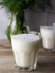 A glass with ayran and dill in the foreground. Glass jug with dill, glass with ayran in the background
