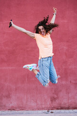 Happy woman wearing sunglasses jumping in front of red wall