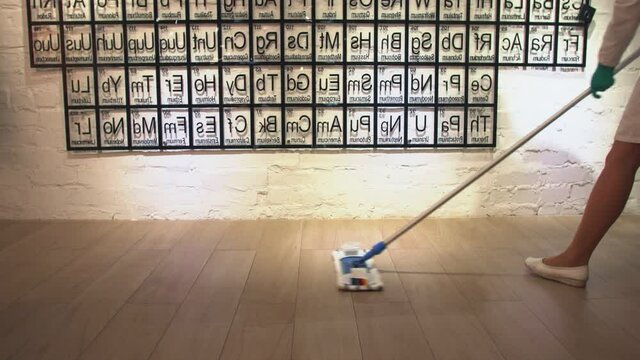 A woman washes the wooden floor with a mop on the background of the periodic table