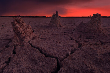 Fototapeta premium Dry lagoon landscape with cracked formations and reddish-colored cloudy skies, Toledo, Spain.