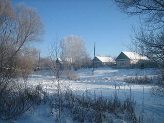 An ordinary Russian village in winter. Houses, sheds, trees, vegetable gardens are covered with snow drifts. The snow is silvered in the sun.Clear blue sky. Cold.