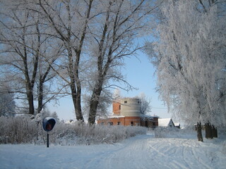 An ordinary Russian village in winter. Houses, sheds, trees, vegetable gardens are covered with snow drifts. The snow is silvered in the sun.Clear blue sky. Cold.