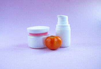 Cream and mask for skin care in white jar and tube with  dispenser near bright juicy tomatoes. Concept Useful Natural Cosmetics from Tomato with Vitamins and Antioxidants.