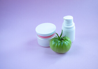 Cream and mask for skin care in white jar and tube with  dispenser near bright juicy tomatoes. Concept Useful Natural Cosmetics from Tomato with Vitamins and Antioxidants.