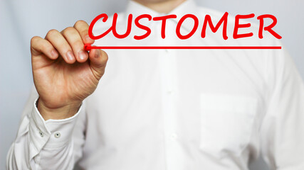 A businessman in a white shirt writes a text CUSTOMER on a white background with a red marker . business concept