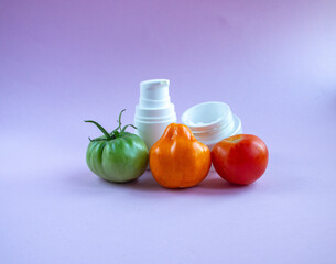 Cream and mask for skin care in white jar and tube with  dispenser near bright juicy tomatoes. Concept Useful Natural Cosmetics from Tomato with Vitamins and Antioxidants.