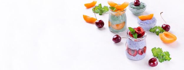 Chia pudding with spirulina and matcha tea powders topped with cherry and apricot in glass jars. Healthy dessert. Web banner with copy space