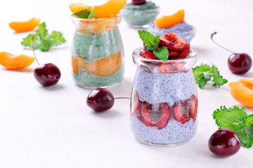 Chia pudding with spirulina and matcha tea powders topped with cherry and apricot and served in glass jars. Healthy dessert