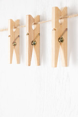three wooden clothespins with a metal spring hang on a rope on a white background. selective focus