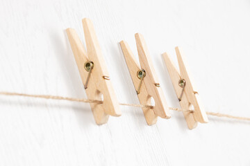 three wooden clothespins with a metal spring hang on a rope on a white background. selective focus