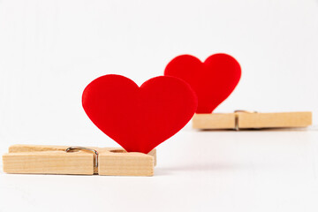 two wooden clothespins hold two red hearts on a white wooden table background close-up. selective focus