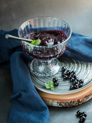 Black currant smoothie, berries  and black currant jam on a grey plate  and black background . 