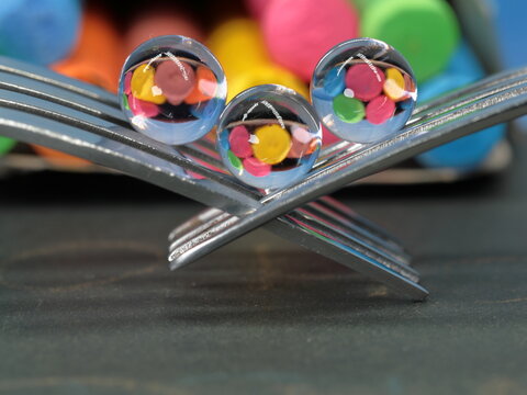 A still life of small transparent balls on forks with a reflection of colored chalks.