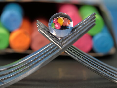 A still life of small transparent balls on forks with a reflection of colored chalks.