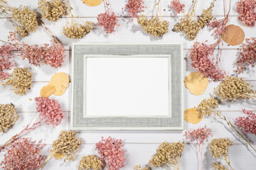 Top view of empty photo frame with dry colorful flowers over a white wooden table - obrazy, fototapety, plakaty