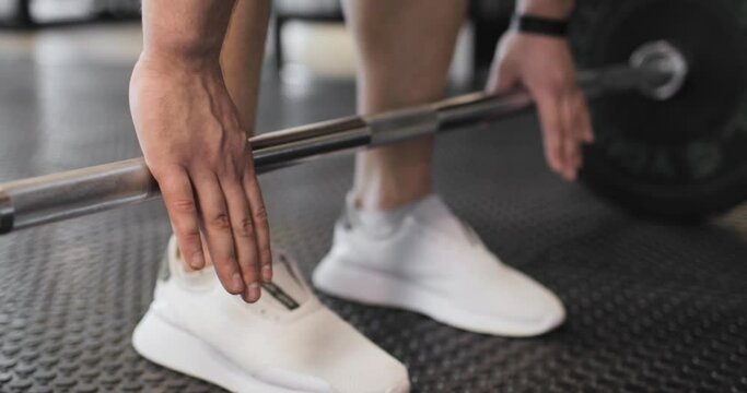Athlete's approach to the bar. Partial view of powerlifter in white sneakers raising barbell. The concept of sports and active lifestyle.
