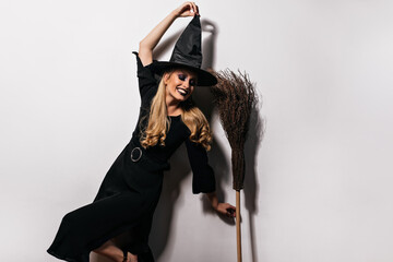 Pleased long-haired witch dancing with broom. Studio portrait of lovable female wizard having fun in halloween.