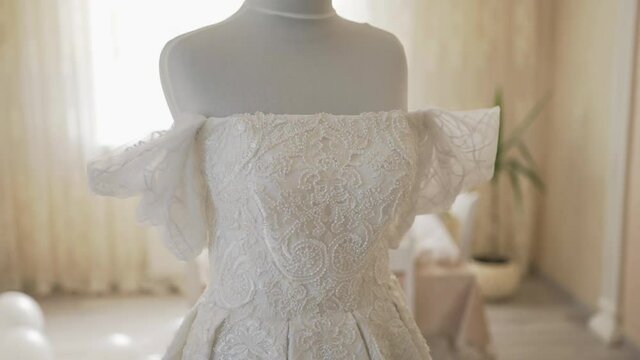 Luxurious lush wedding dress on a mannequin in the room. Clothes for bride. Expensive wedding dress made of beautiful fabric. Wedding dress with ruffled sleeves and sewn lace on the corset and skirt