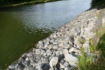Fototapeta na wymiar Slope stabilization of an artificial waterway Midland Canal (Mittellandkanal) in Germany by using natural stones and wire mesh. Hannover, Lower Saxony, Germany. 