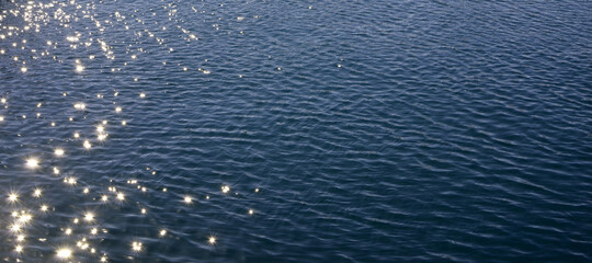 Blue sea water with sun reflections and ripples. Blue sea water surface with ripples and sun reflections. Sparks from the sun's reflection on the blue surface of rippled sea water.