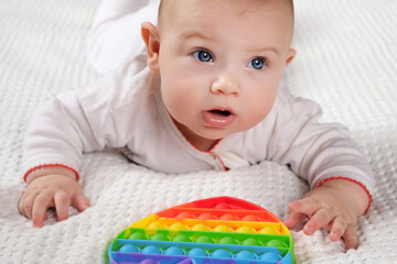Happy Kid Playing with Pop It. Newborn Baby Playing with Simple Dimple. The Flexible Sensory Fidget Push-Bubble Toy is Good for Baby Development. Little Child Holds an Eternal Bubble in her Mouth.