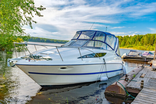 A beautiful summer landscape with a blue sky, a forest on the river, a yacht is moored at the pier. The concept of a boat trip, sailing on the sea on a ship.