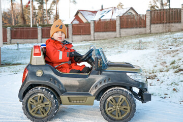 Fototapeta na wymiar Smiling boy in red overalls and yellow hat is driving a car