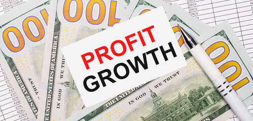 Against the background of reports and dollars - a white pen and a card with the text PROFIT GROWTH. Business concept