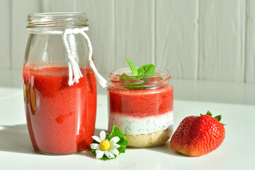 Homemade multi-layer dessert with strawberry and cream cheese in a glass jar. Ripe fresh green lime and mint on white background.