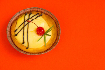 Round cake with a cherry in the middle on a bright orange background. On the right is a copy space. Delicious dessert with berries. selective focus
