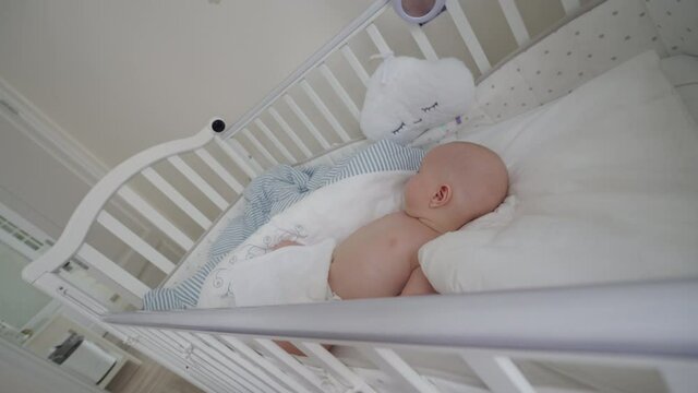 Baby boy sleeping in a crib with installed IP wireless security camera as baby monitor, interior of a modern apartment bedroom. High quality 4k footage